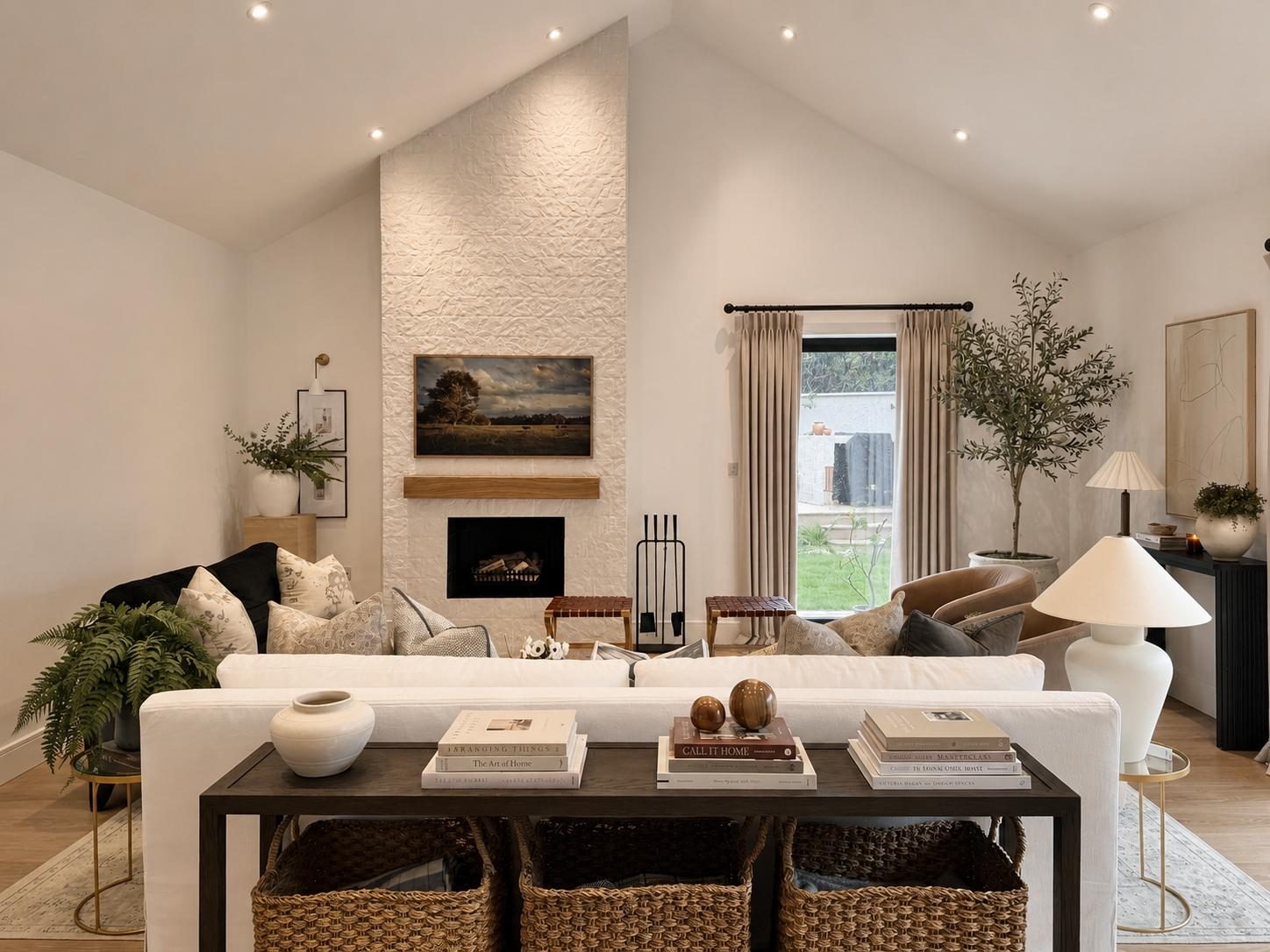 Living room with vaulted ceiling, textured white chimney breast, white sofas and console table with woven baskets